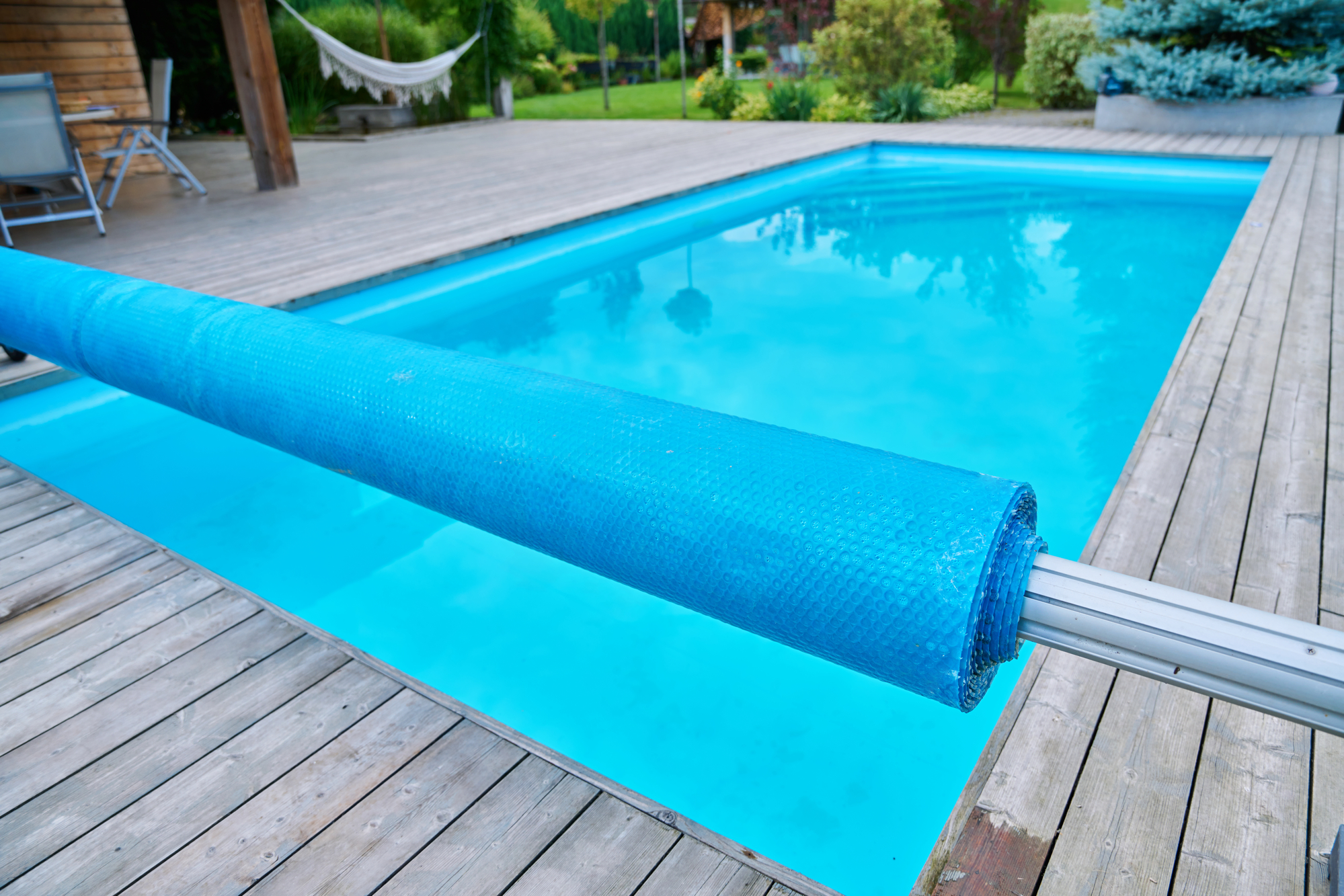 Swimming pool with a blue bubble cover partially rolled up on the deck