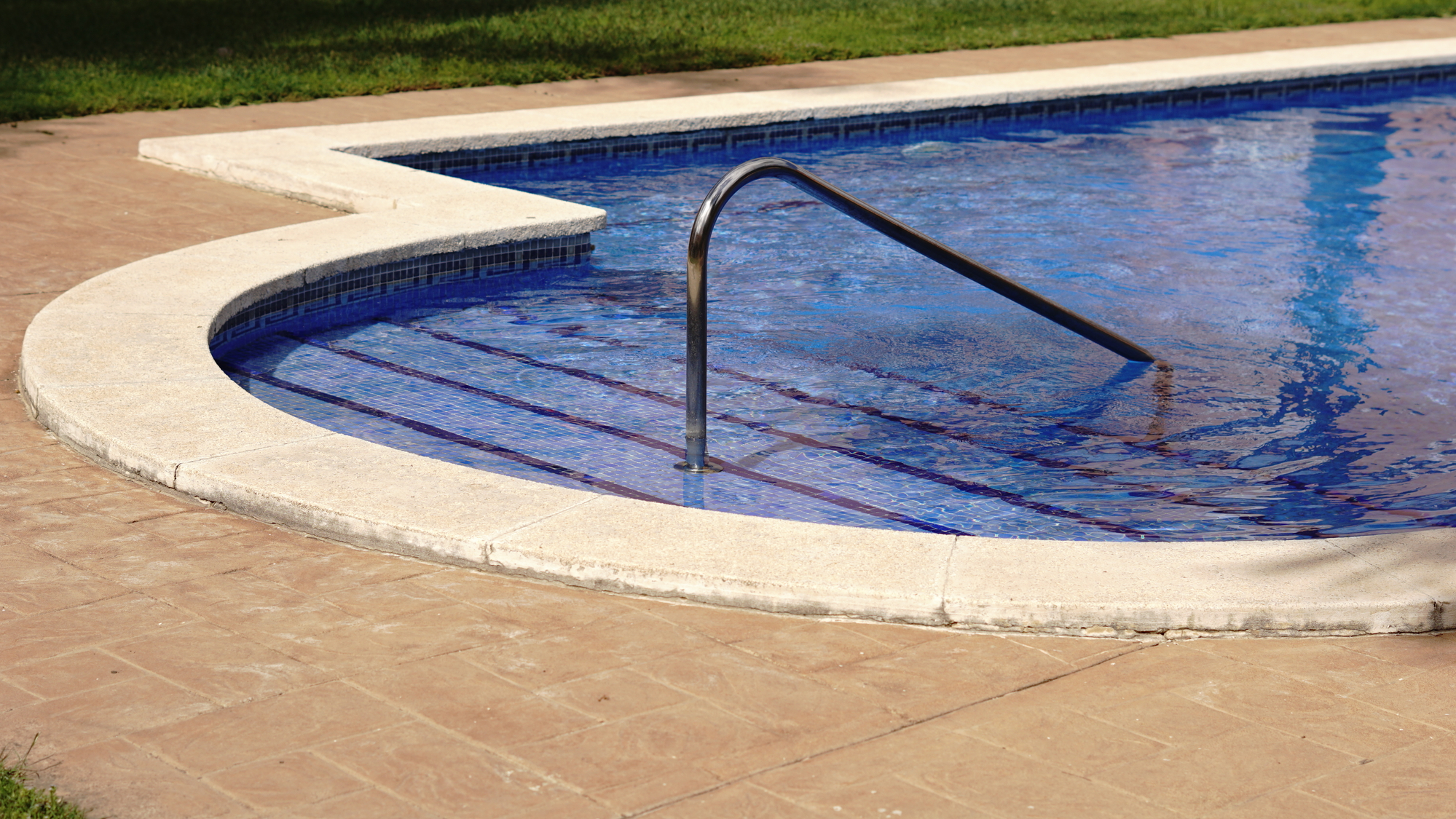 A close-up view of a swimming pool's edge with a stainless steel ladder leading into the clear, shimmering blue water